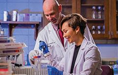 Man and woman working in lab in white coats looking at beakers.